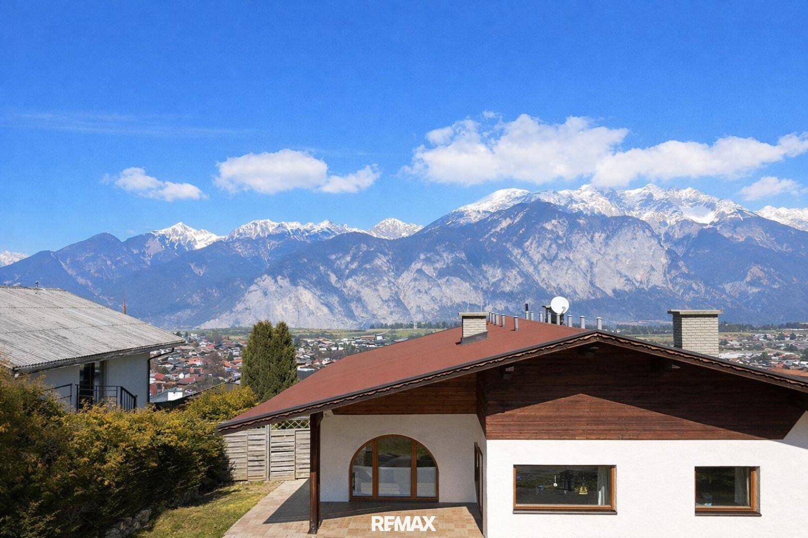 Ansicht des Hauses mit braunem Dach und Holzelementen vor einer beeindruckenden Bergkulisse.