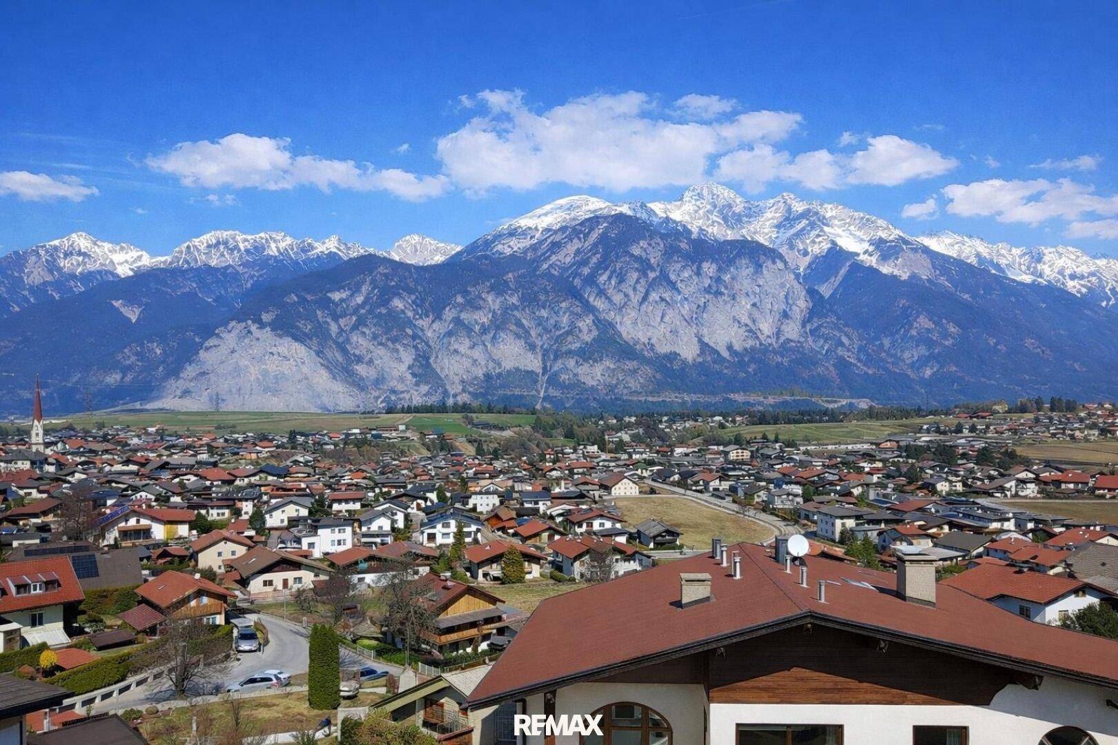 Weitläufiger Blick über eine Siedlung mit vielen Häusern und die majestätischen Berge am Horizont.