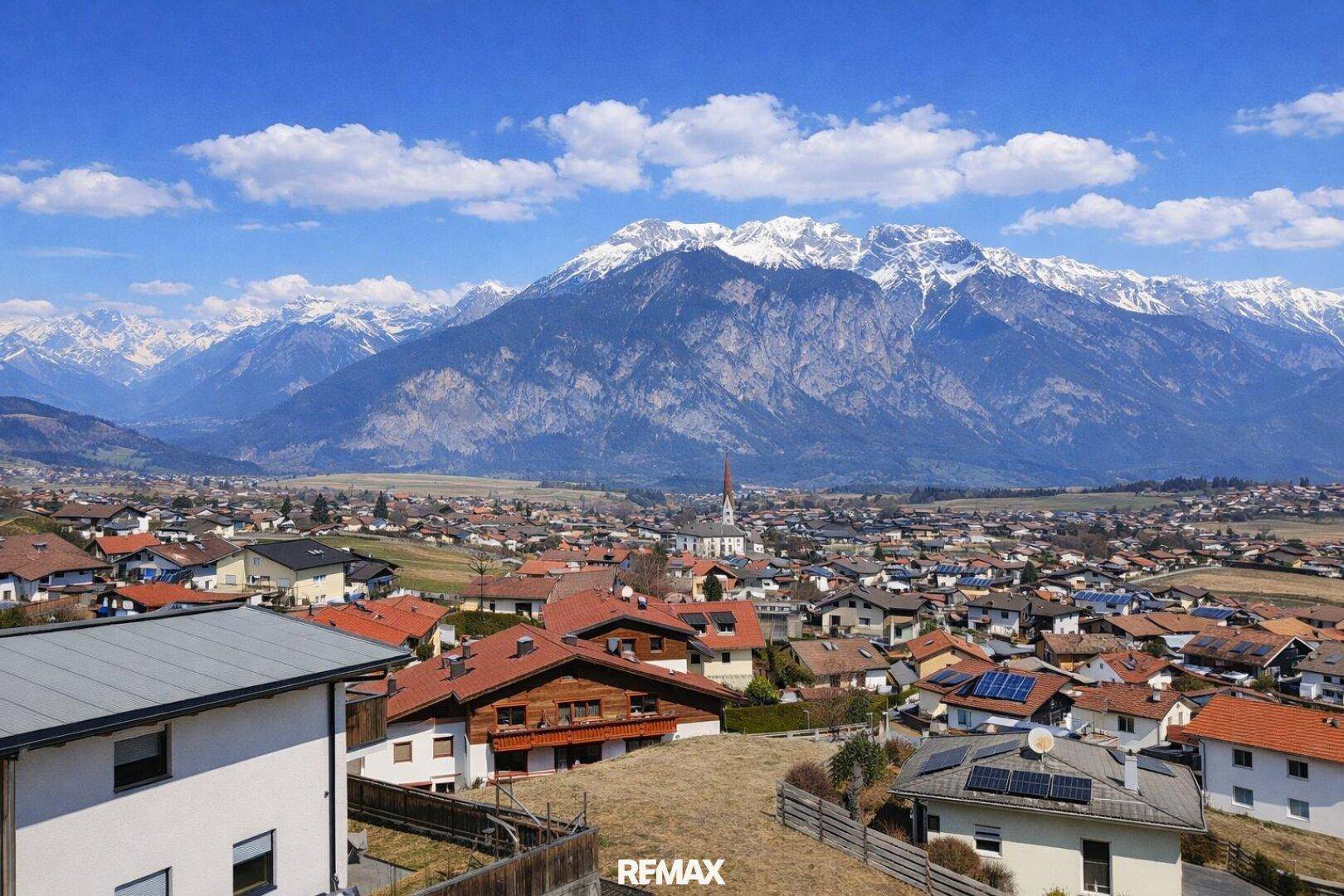 Panoramablick über eine malerische Stadt mit roten Dächern und einer beeindruckenden Bergkette im Hintergrund.