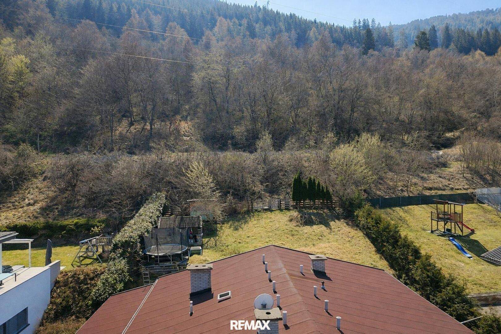 Dachansicht des Hauses mit Blick auf den weitläufigen Garten und die bewaldeten Hügel im Hintergrund.