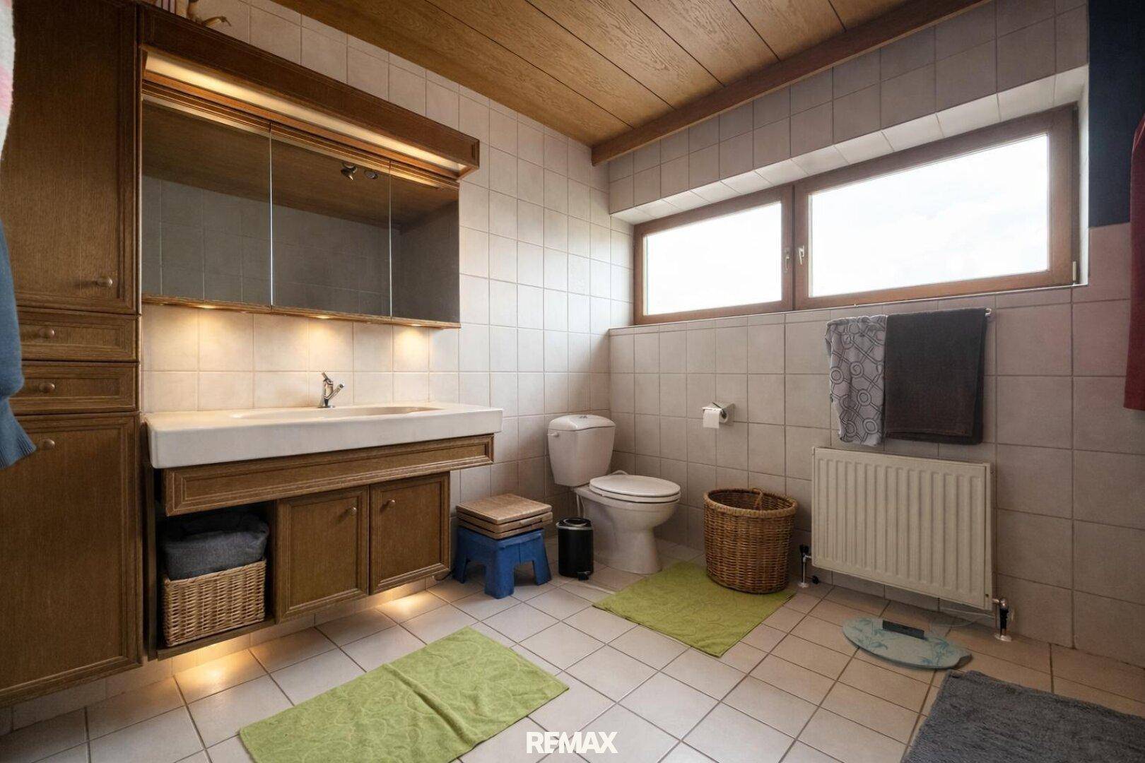 Badezimmer mit Holzdecke, Fliesenboden und großem Fenster, gut gepflegt und hell.