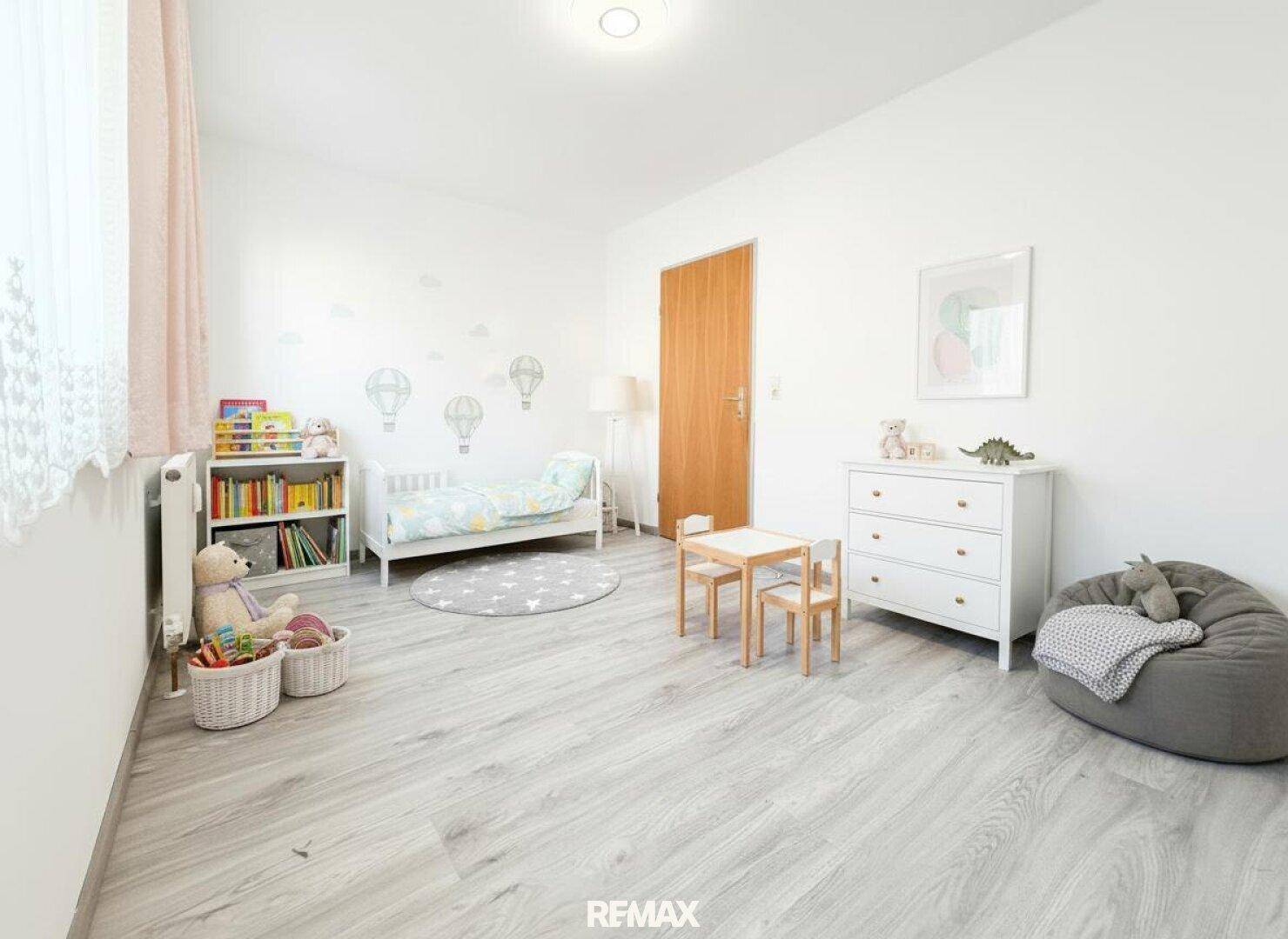 Freundliches Kinderzimmer mit hellem Laminatboden, kleinem Bett und Spielbereich.