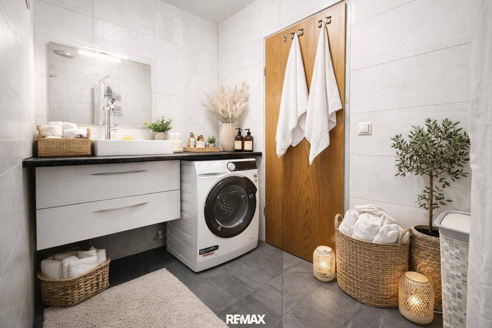 Modernes Badezimmer mit Dusche, Waschbecken, Waschmaschine und dunklen Fliesen.