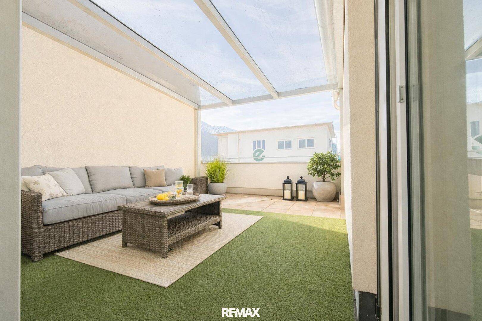Überdachte Terrasse mit bequemen Loungemöbeln und Blick auf die umliegende grüne Landschaft.