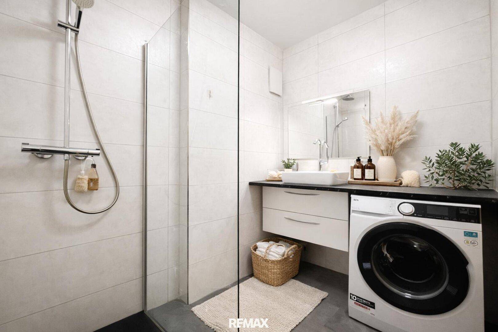 Modernes Badezimmer mit ebenerdiger Dusche, Waschbecken und integrierter Waschmaschine für Komfort.