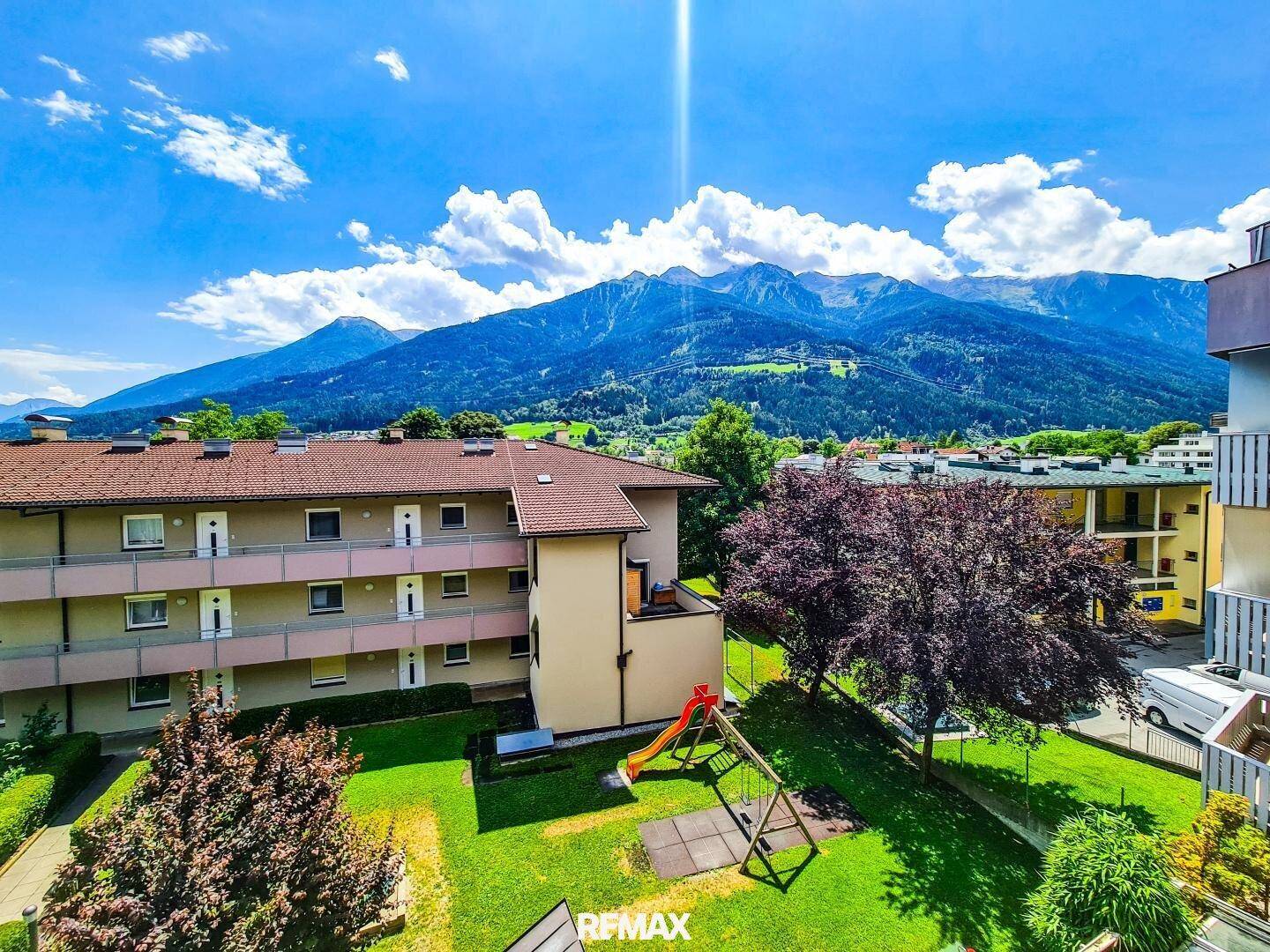 Wohngebäude mit Spielplatz im Innenhof und beeindruckendem Blick auf die umliegende Berglandschaft.