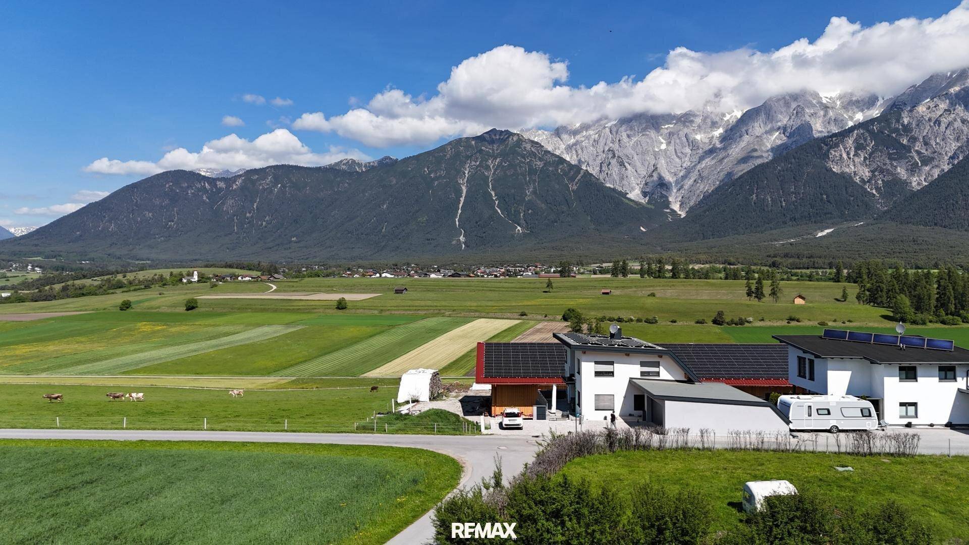 Panoramablick auf Häuser, Felder und majestätische Berge unter einem weiten Himmel.