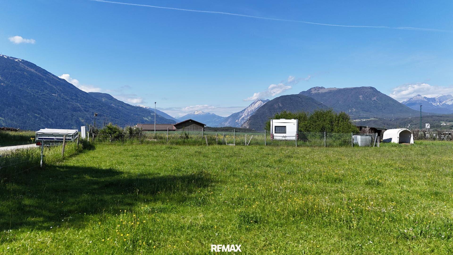 Weitläufige grüne Felder mit Bergen im Hintergrund unter einem strahlend blauen Himmel.