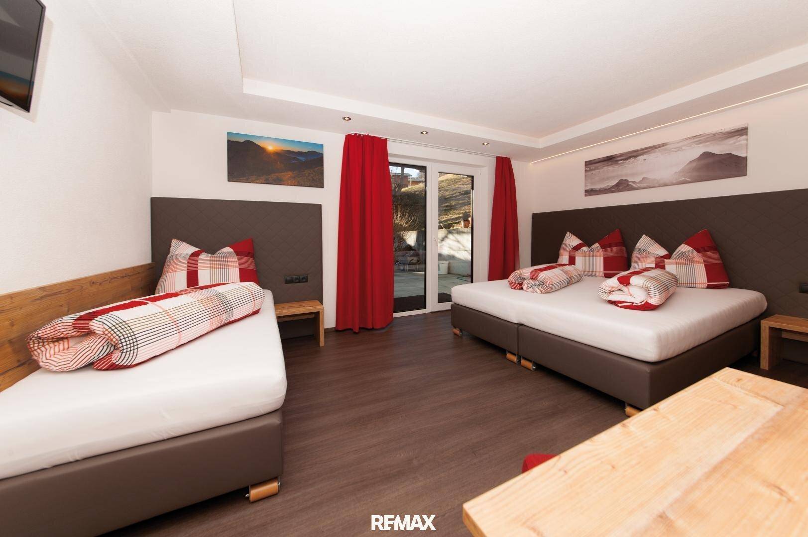 Gemütliches Schlafzimmer mit Doppelbett, Einzelbett und Zugang zu einem Balkon oder einer Terrasse.