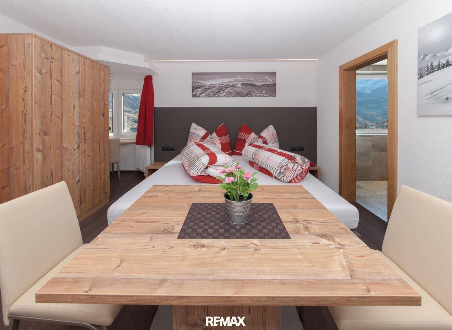 Helles Schlafzimmer mit Doppelbett, Holztisch und Stühlen, sowie einem Fenster mit Bergblick.