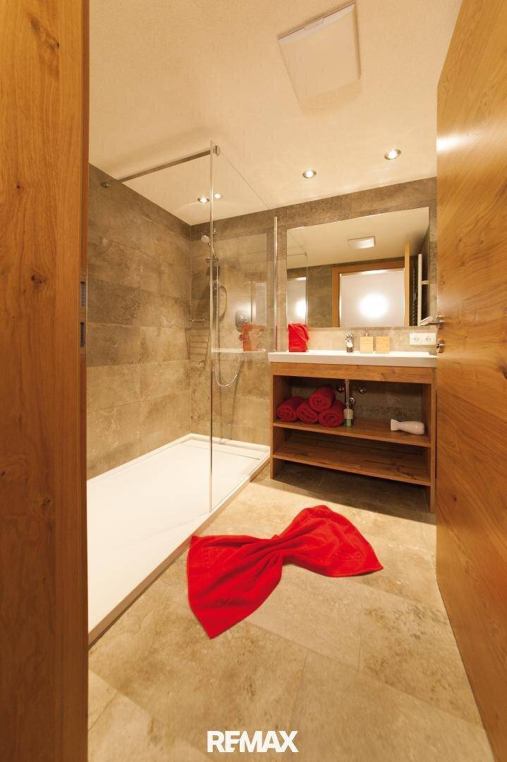 Modernes Badezimmer mit begehbarer Dusche, Holzwaschtisch und hellen Fliesen an Wänden und Boden.
