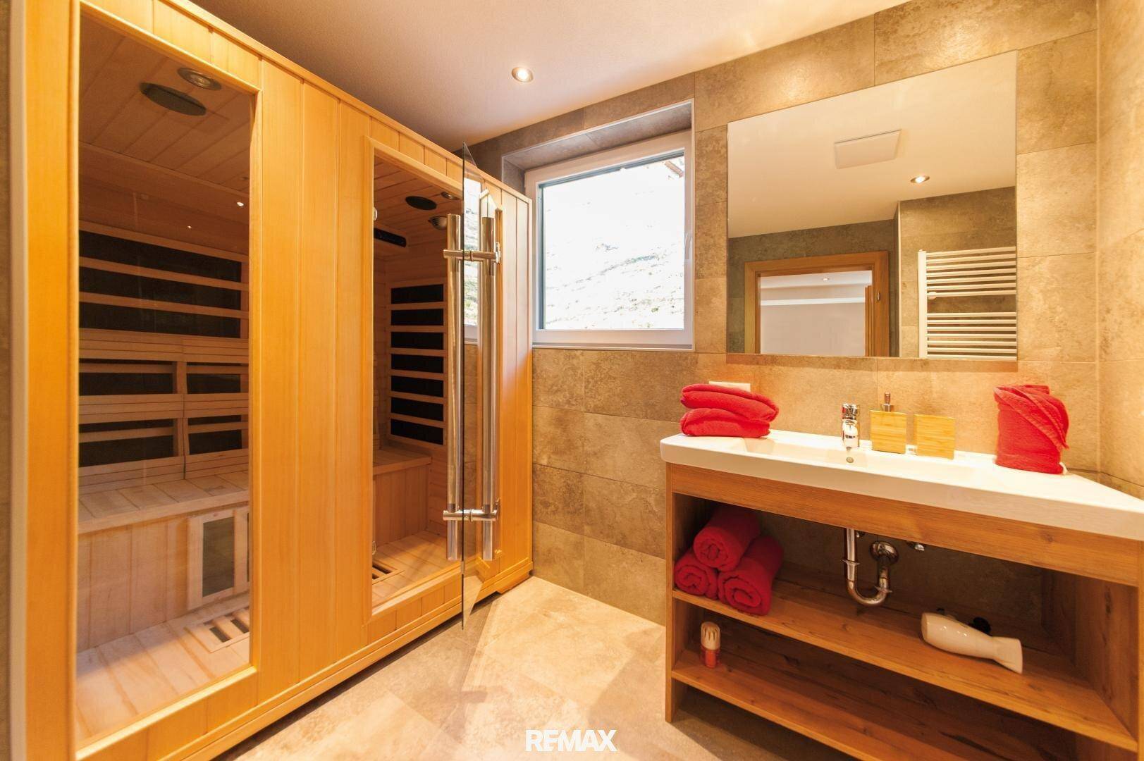 Modernes Badezimmer mit integrierter Sauna, Holzwaschtisch und Fenster mit Bergblick.