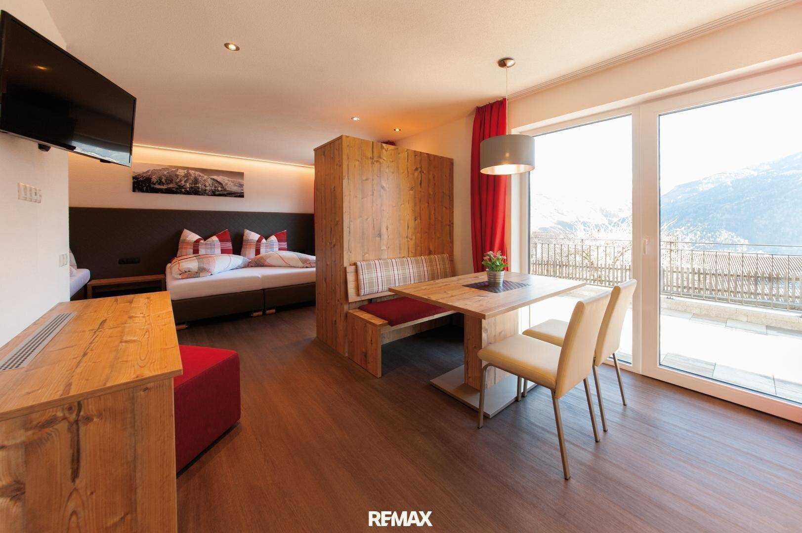 Helles Schlafzimmer mit integriertem Essbereich, Holzelementen und Zugang zu einem Balkon mit Bergblick.