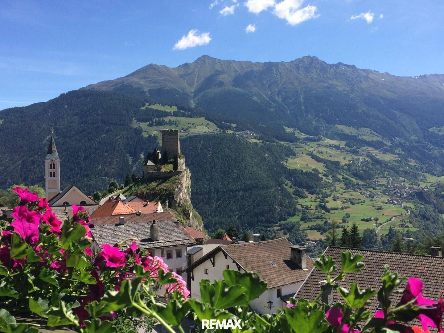 Malerischer Panoramablick auf eine Berglandschaft mit historischem Dorf und Burgruine.