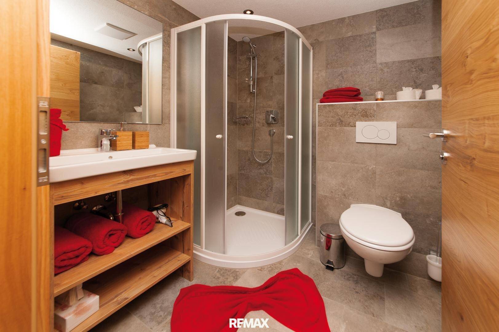 Funktionales Badezimmer mit Duschkabine, wandhängendem WC und Holzwaschtischunterschrank.