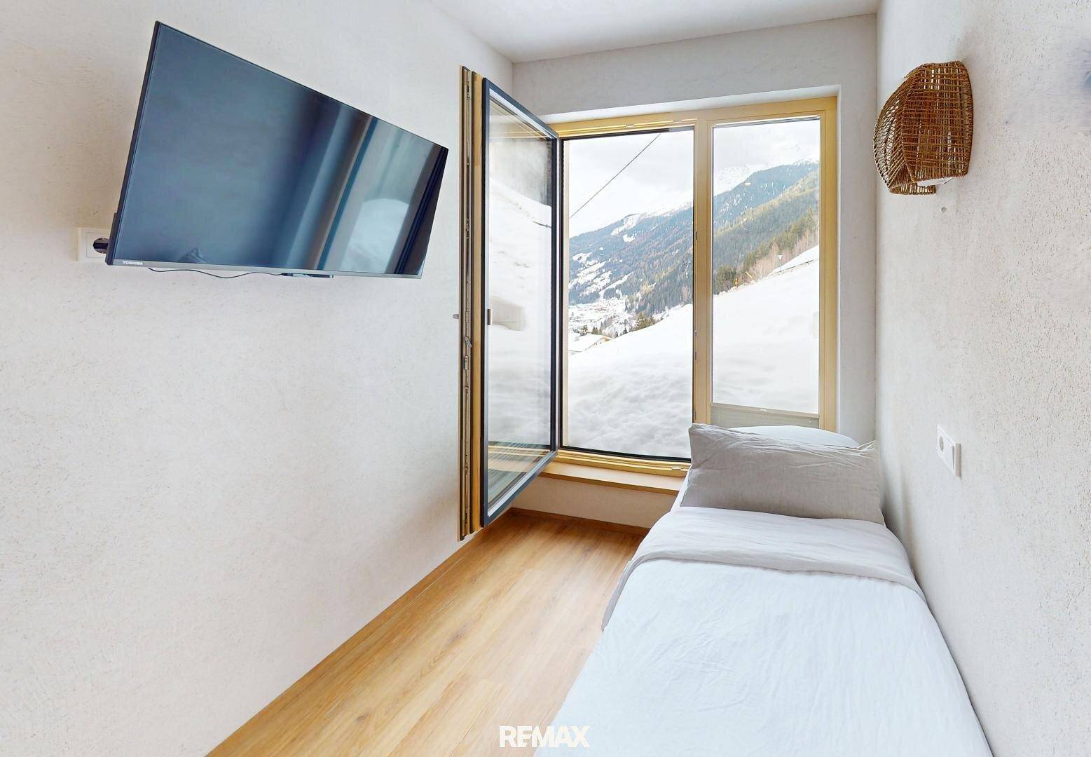 Helles Einzelzimmer mit Wandfernseher, Holzboden und Fenster mit Bergblick.