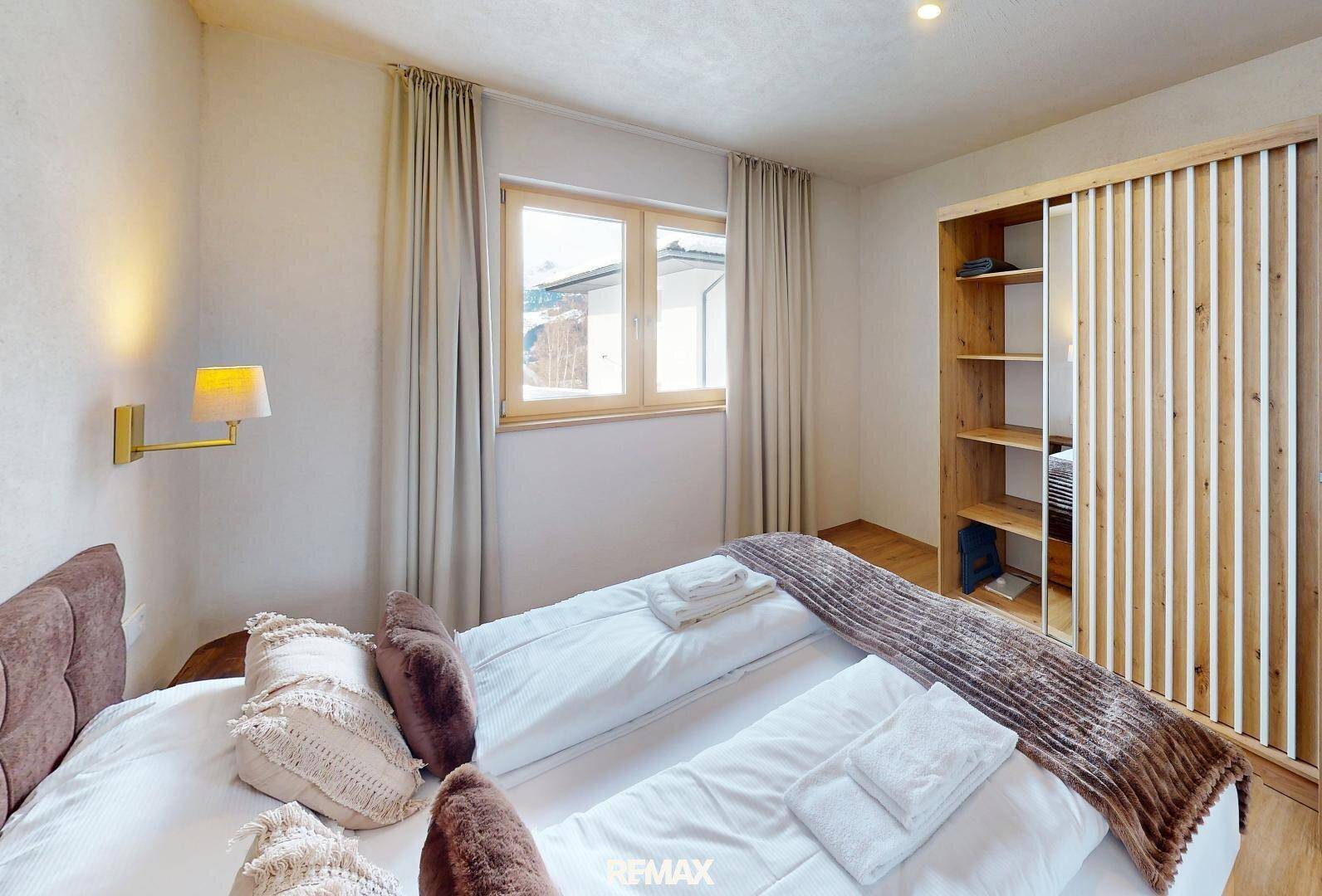 Gemütliches Schlafzimmer mit Doppelbett, Holzboden und einem Kleiderschrank mit Holzlamellen.