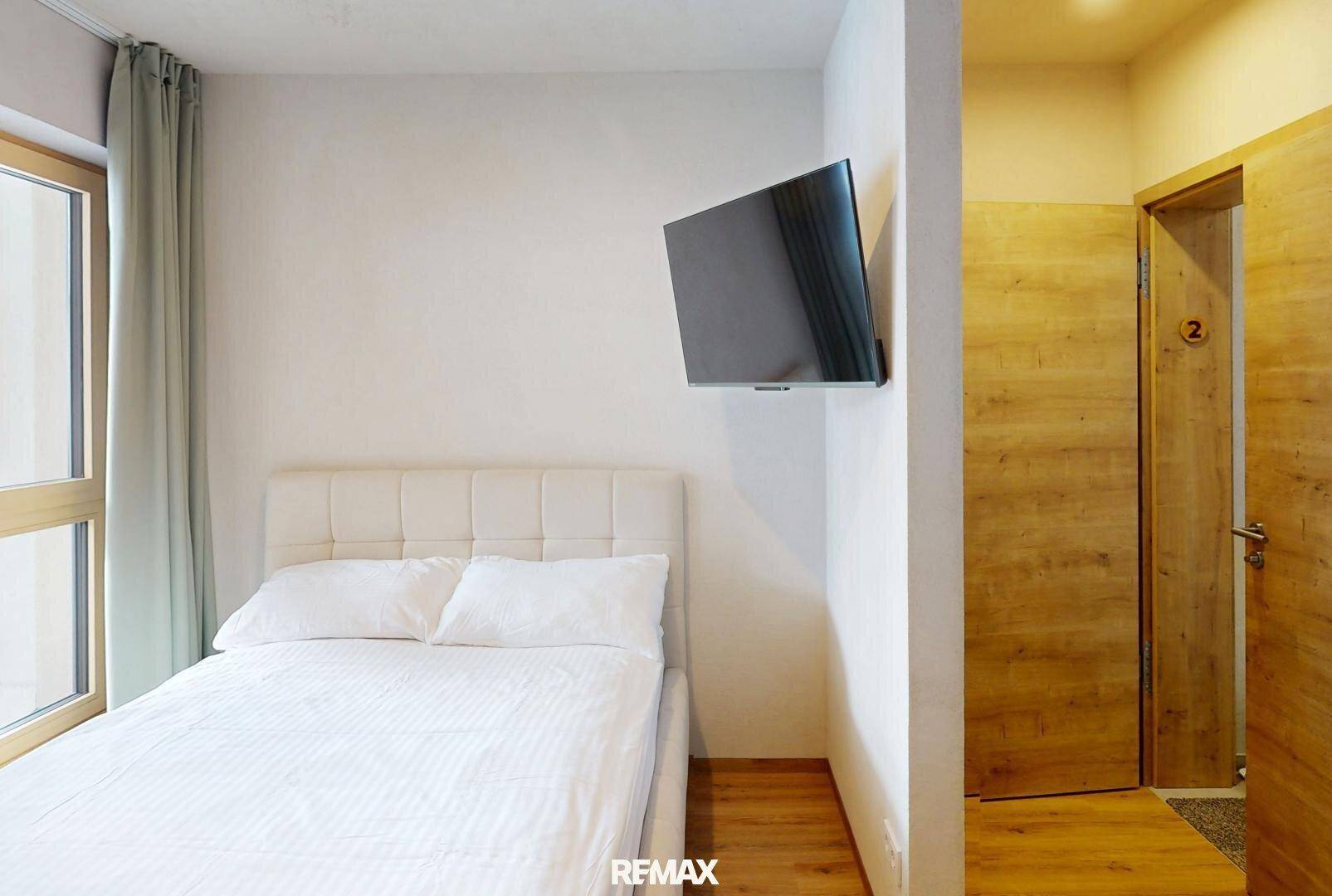 Gemütliches Schlafzimmer mit Einzelbett, Wandfernseher und Zugang zu einem weiteren Raum.