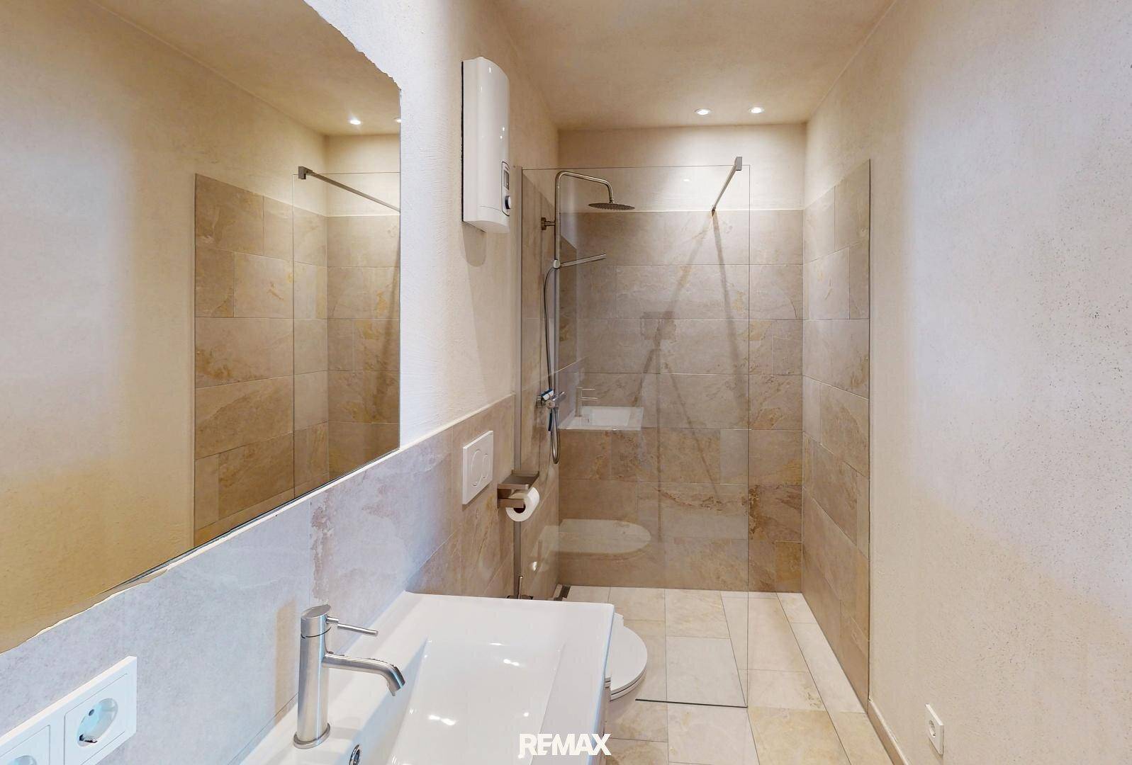 Modernes Badezimmer mit großer Spiegelfläche, wandhängendem WC und begehbarer Dusche.