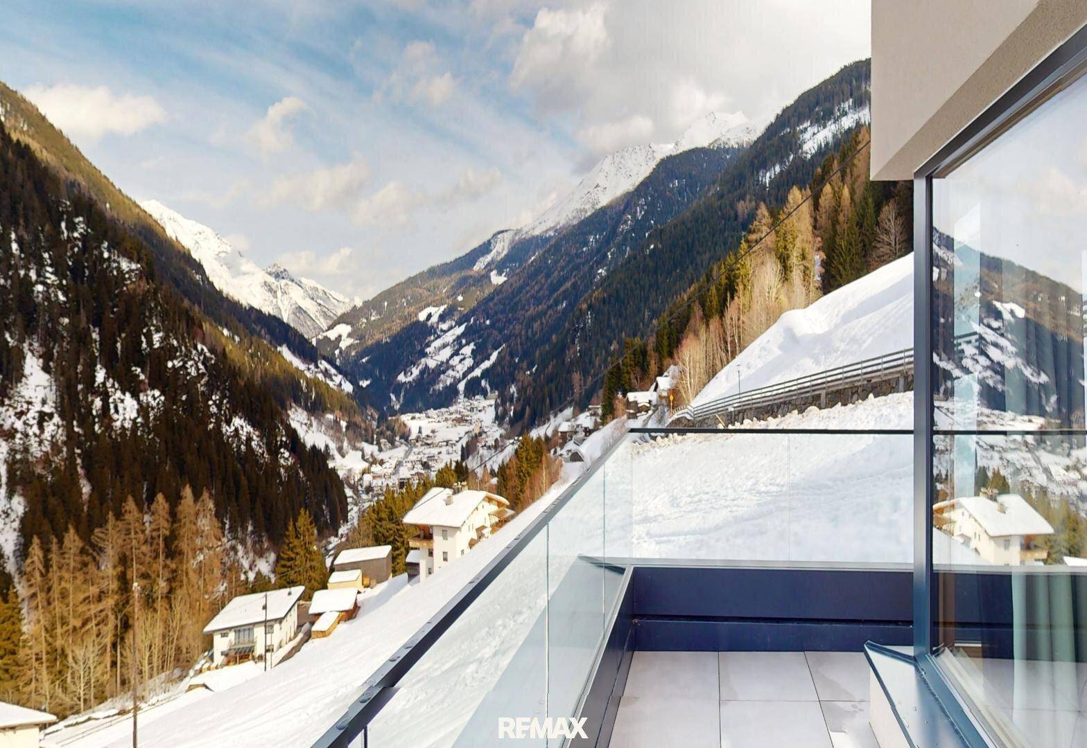 Geräumiger Balkon mit Glasgeländer und weitem Blick auf die verschneite Berglandschaft.