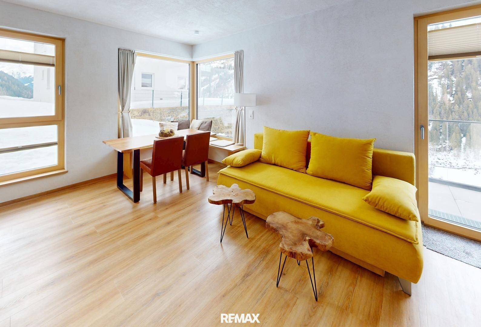 Heller Wohn- und Essbereich mit gelbem Sofa, Holztisch und Zugang zum Balkon.
