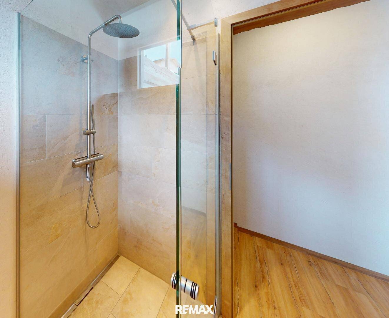 Moderne begehbare Dusche mit Regenduschkopf und großformatigen Fliesen.