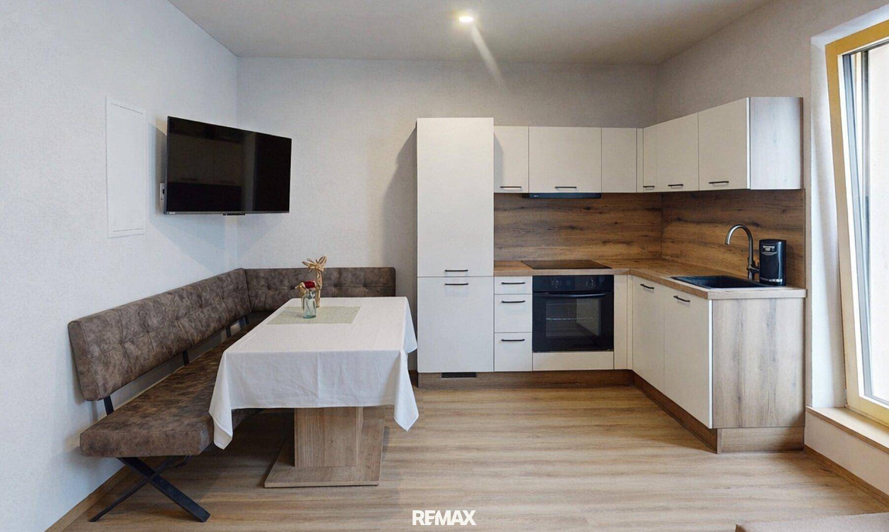 Moderne Küche mit Eckbank, Esstisch und weißen Schränken in Kombination mit Holzelementen.