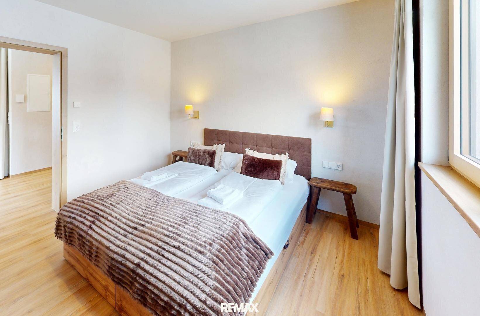 Helles Schlafzimmer mit Doppelbett, Holzboden und schlichten Wandleuchten für eine angenehme Atmosphäre.