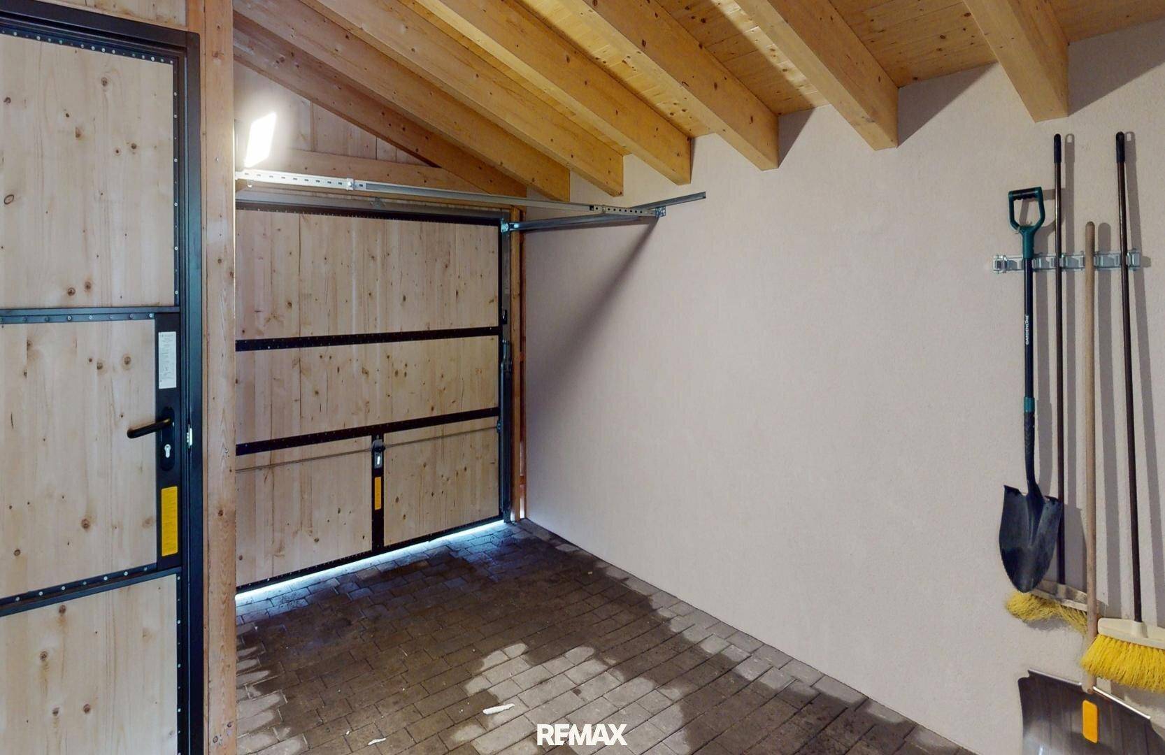 Geräumige Garage mit Holztor und offenem Dachstuhl, bietet Platz für ein Fahrzeug.
