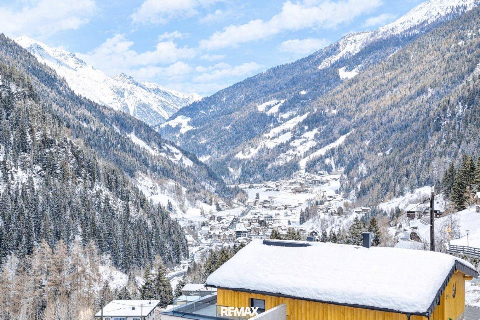 Panoramablick auf ein verschneites Tal mit traditionellen Häusern und majestätischen Bergen.