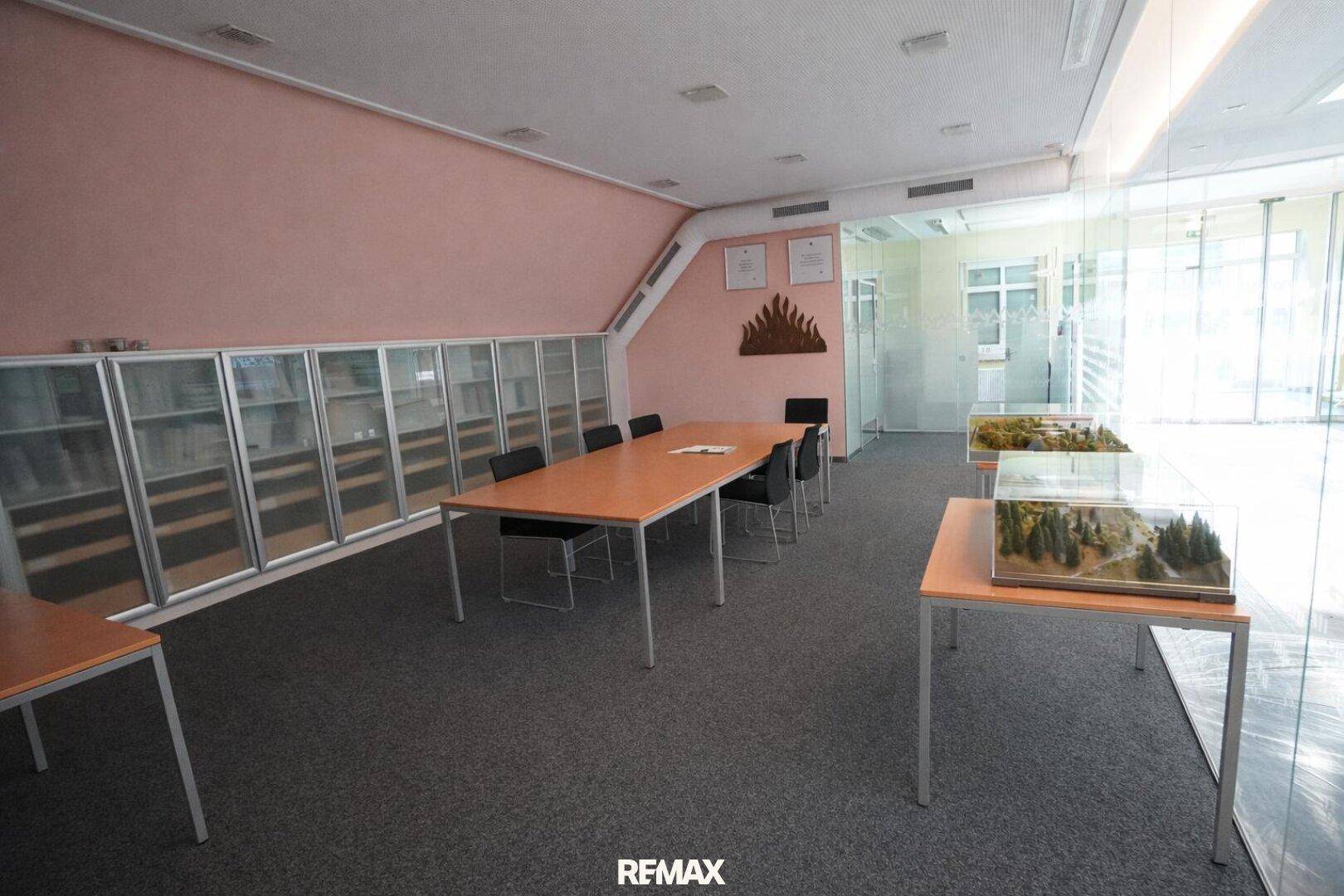 Besprechungsraum oder Bibliothek mit langem Tisch, Stühlen und Vitrinen mit Modellen.