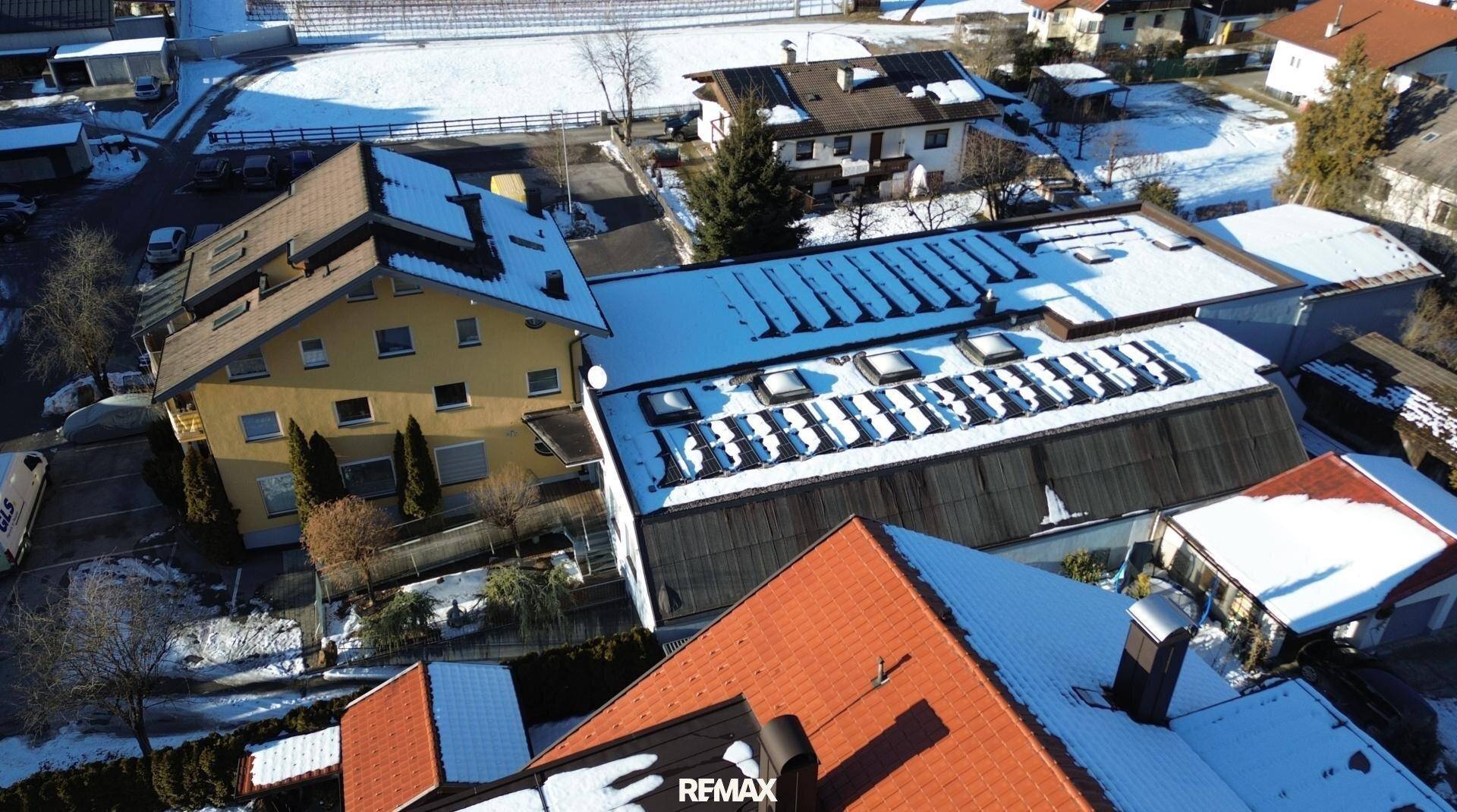 Dachlandschaft eines Gebäudekomplexes mit Photovoltaikanlage und verschneiten Dächern.