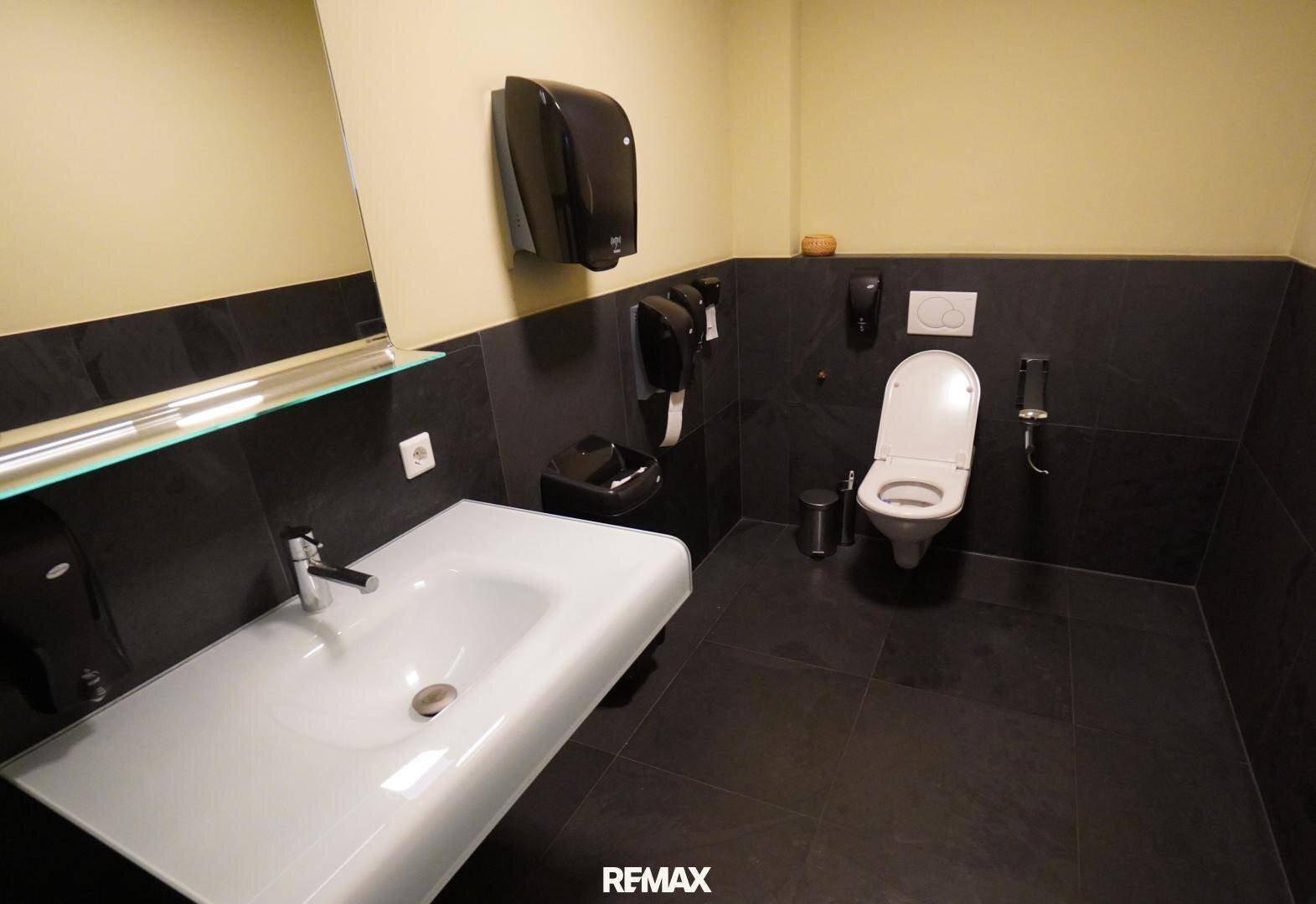 Modernes WC mit dunklen Fliesen, wandhängender Toilette und breitem Waschbecken.