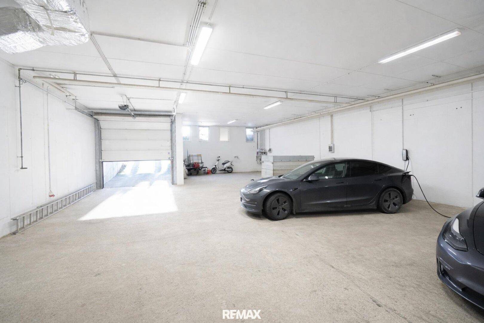 Geräumige Garage mit Betonboden, Elektroauto-Ladestation und großem Rolltor.