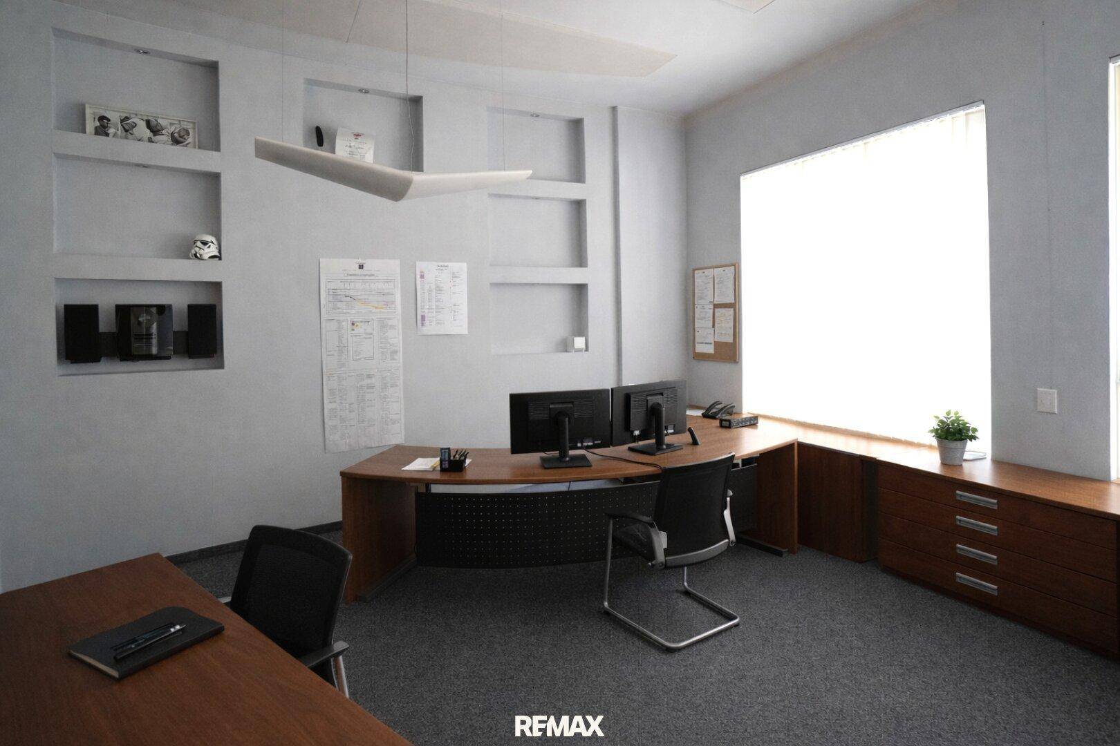 Modernes Büro mit großem Schreibtisch, Computern und integrierten Wandregalen.