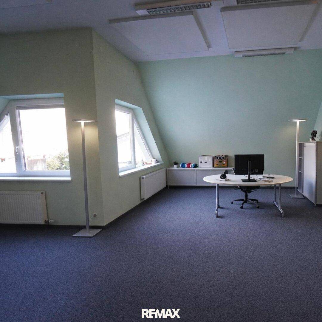 Helles Dachgeschossbüro mit schrägen Wänden, rundem Schreibtisch und großen Fenstern.