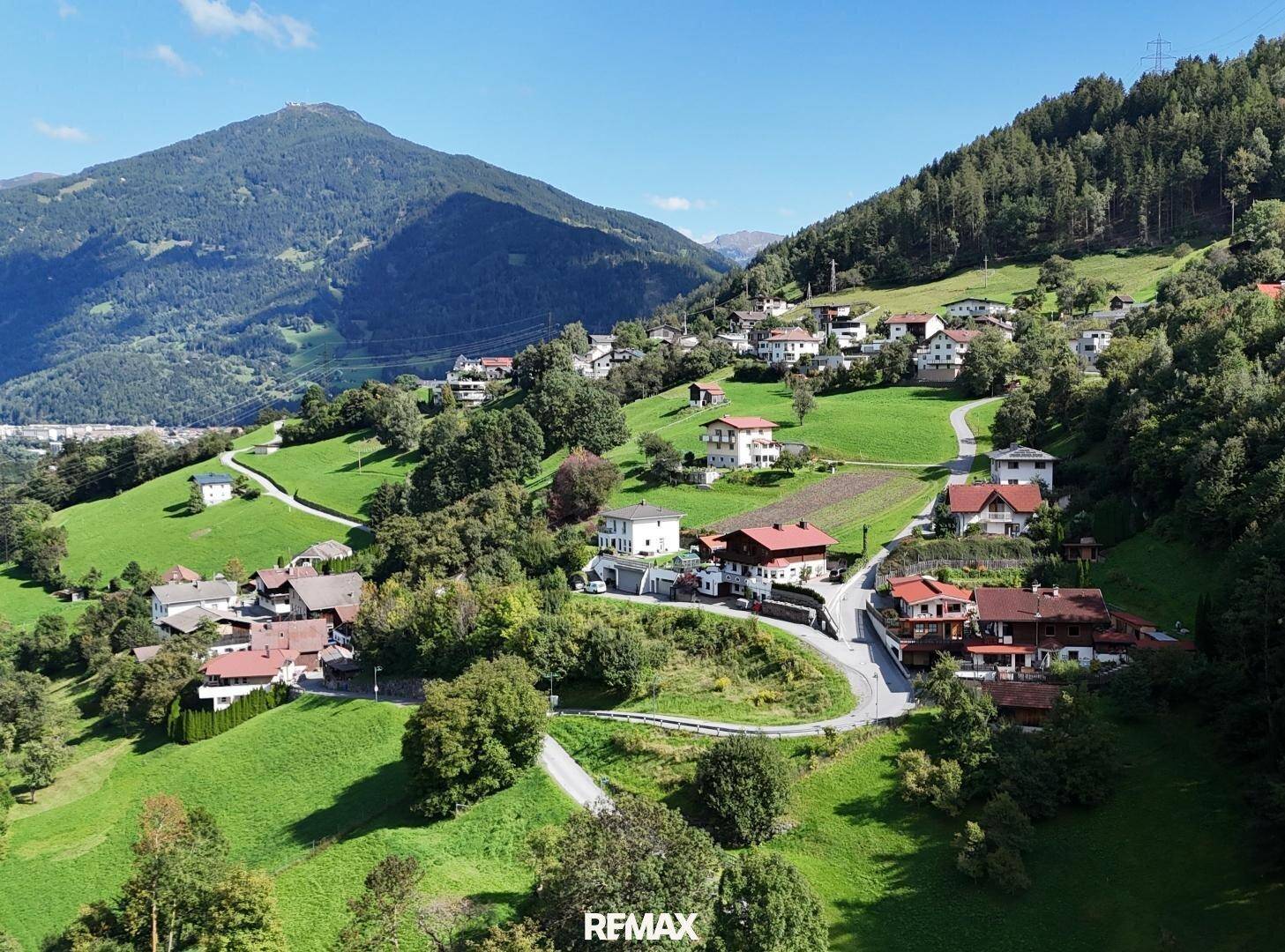 Weitläufige Luftaufnahme eines Bergdorfes in einer grünen Landschaft unter blauem Himmel.