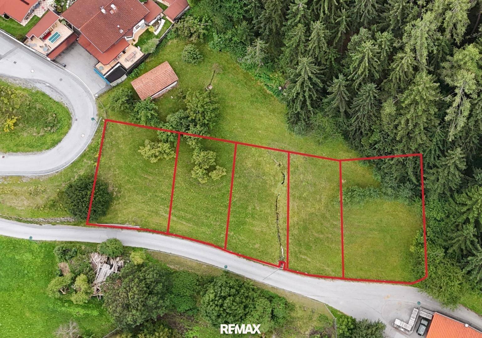 Luftaufnahme mehrerer parzellierter Grundstücke mit roter Umrandung, eingebettet in eine grüne Landschaft.