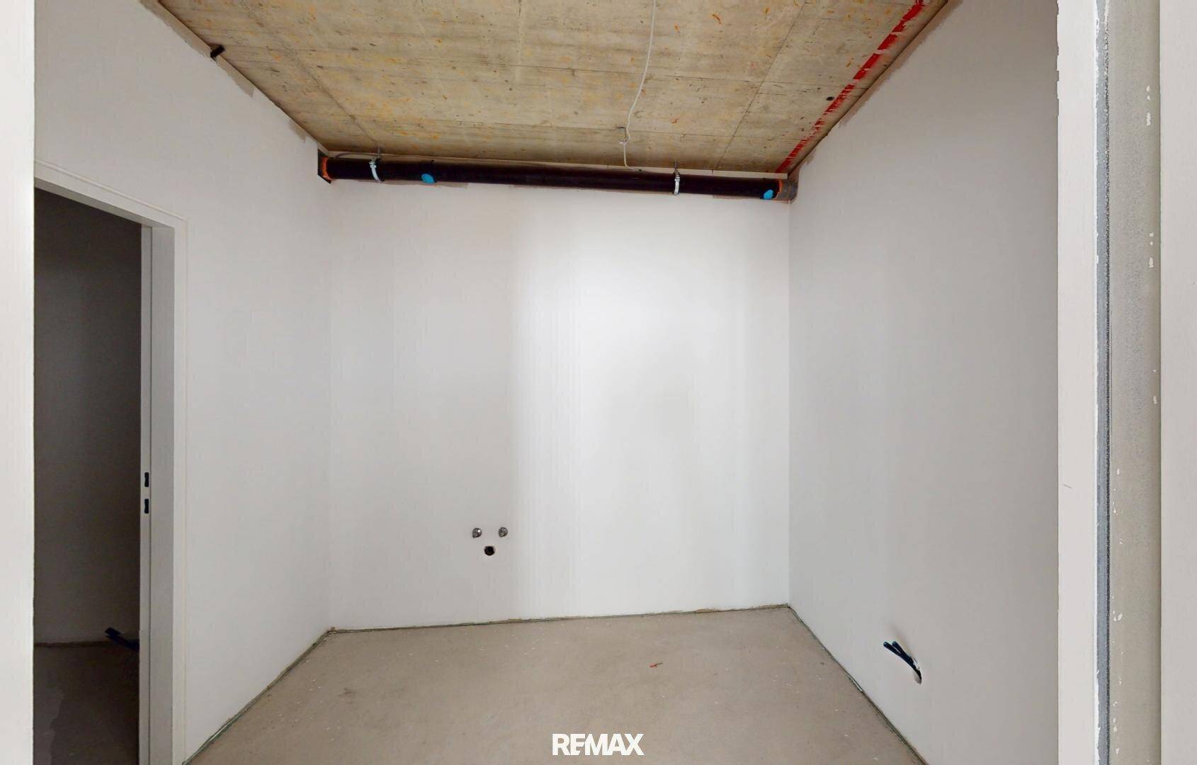 Kleiner, unfertiger Raum mit weißen Wänden, sichtbarer Betondecke und Installationsvorbereitungen.
