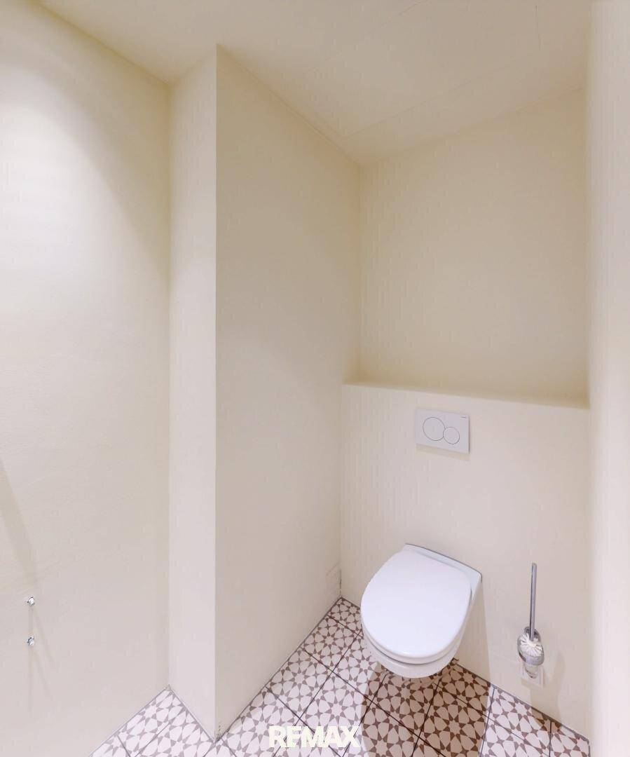 Modernes Gäste-WC mit Wand-WC und gemusterten Fliesen, in einem hellen und sauberen Zustand.