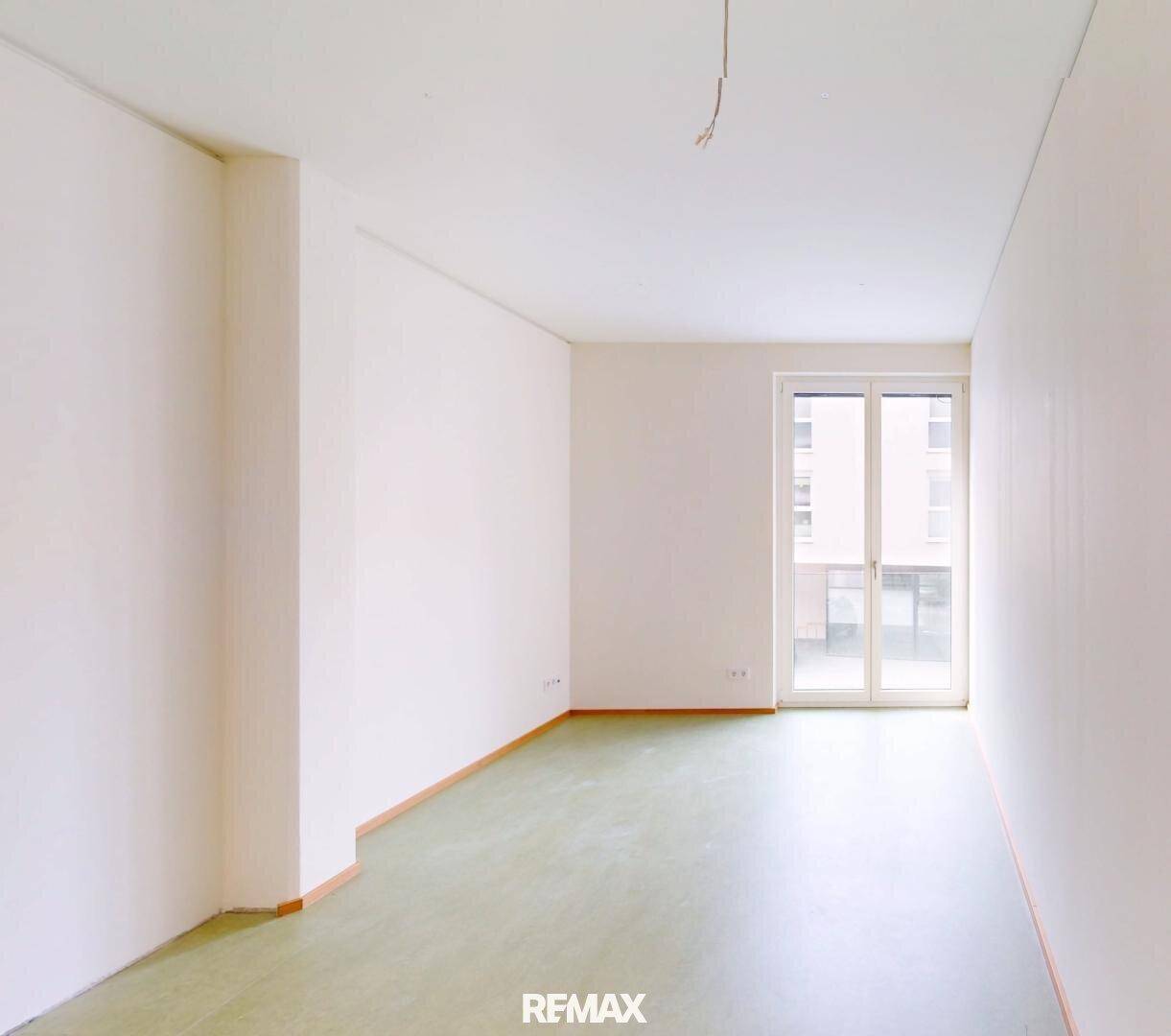 Heller, leerer Raum mit grünem Bodenbelag und einer großen Fenstertür, die Tageslicht spendet.