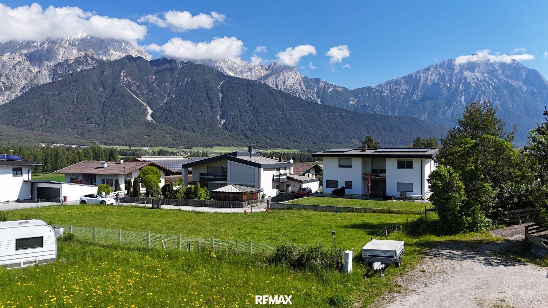 Häuser in einer ländlichen Umgebung mit majestätischen Bergen im Hintergrund unter blauem Himmel.