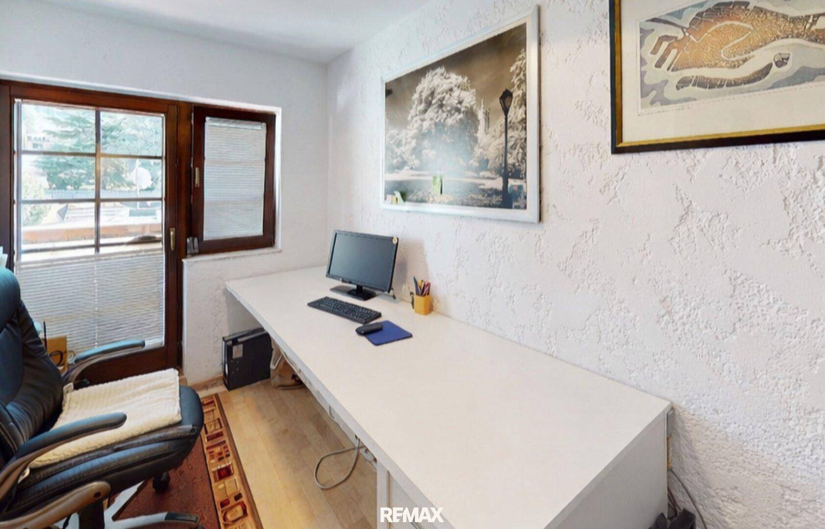 Helles Arbeitszimmer mit langem Schreibtisch, Bürostuhl und Zugang zum Außenbereich.