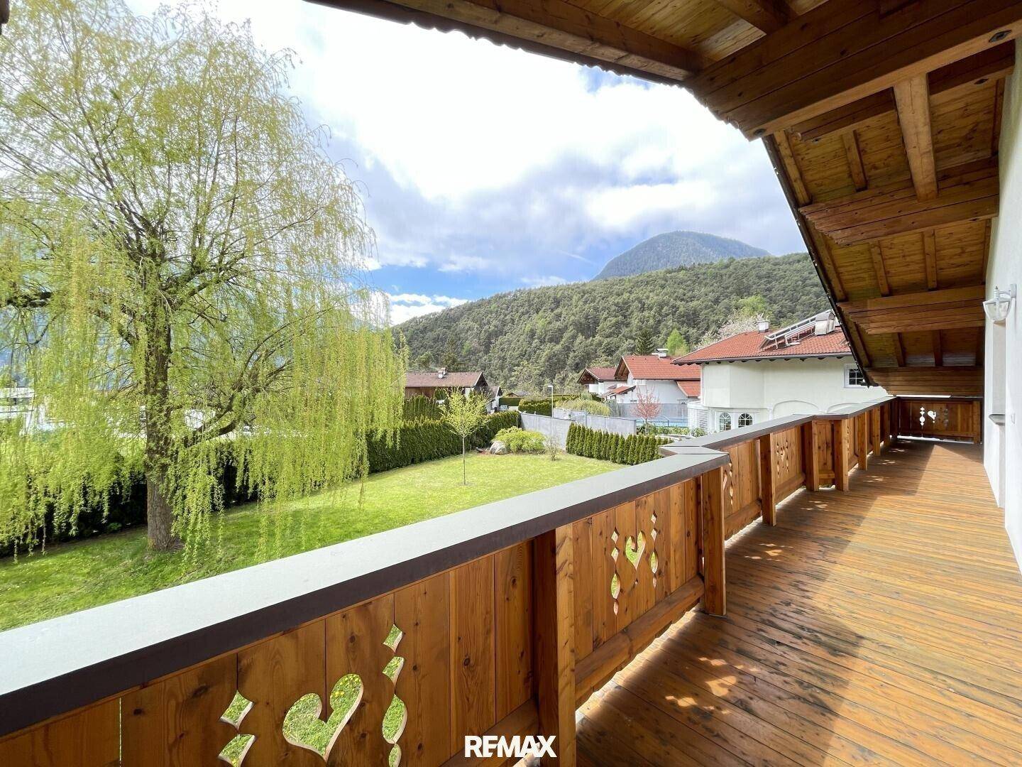 Langer Holzbalkon mit traditionellem Geländer und weitem Blick auf die Berge.