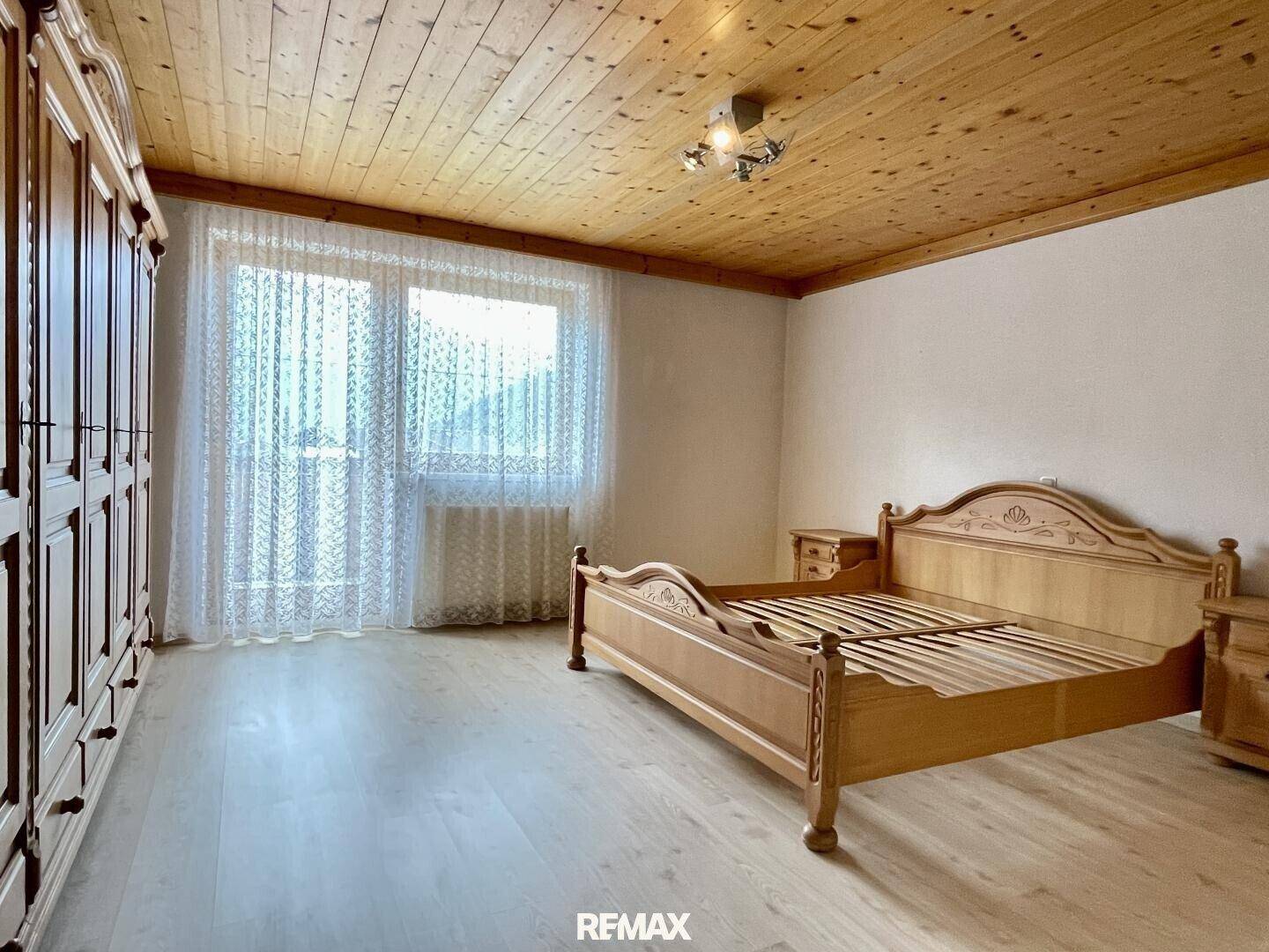 Helles Schlafzimmer mit Holzmöbeln, großem Fenster und Holzbalkendecke.