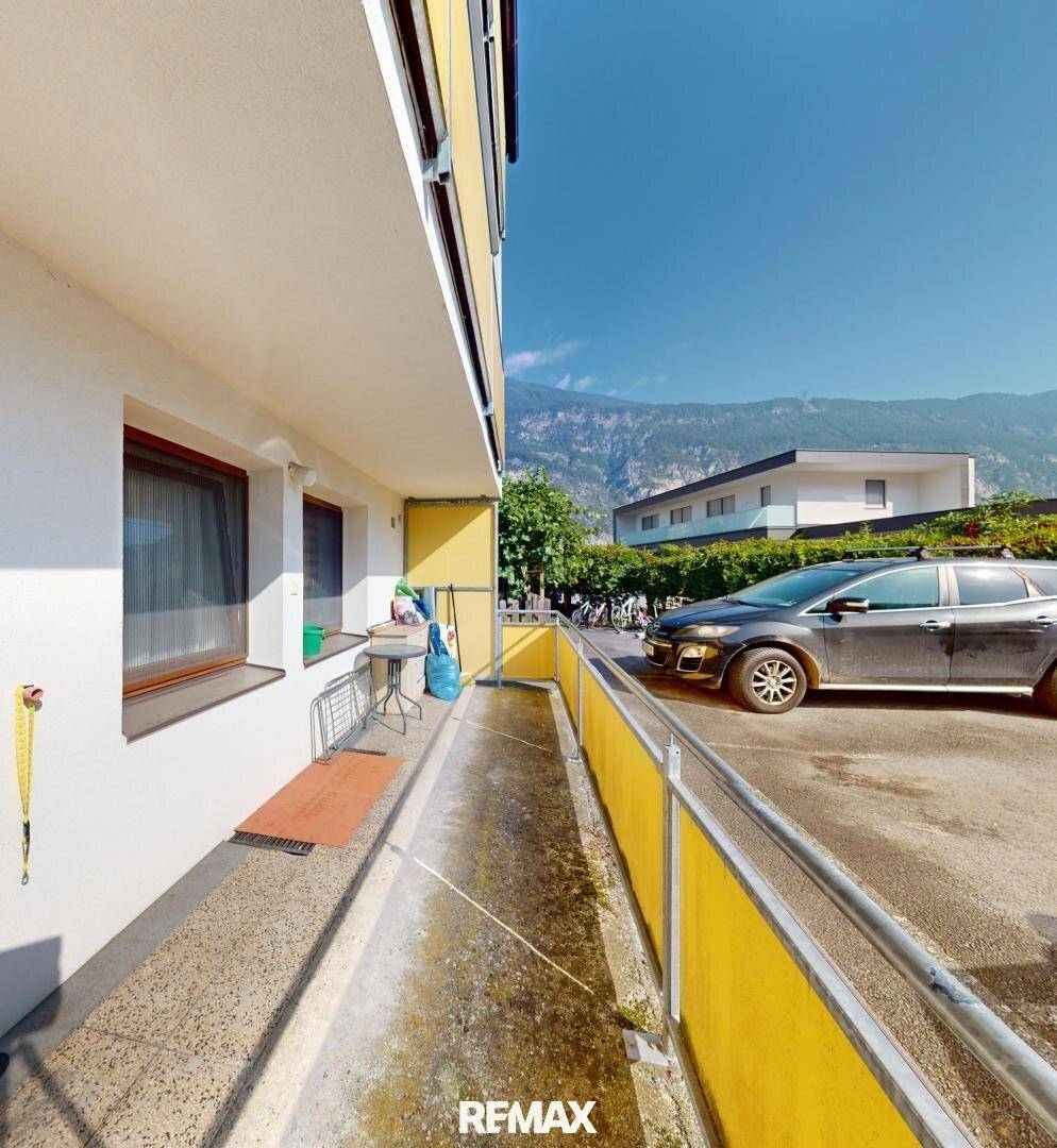 Langer Balkon oder Terrasse im Erdgeschoss mit gelbem Geländer und Parkplatz.
