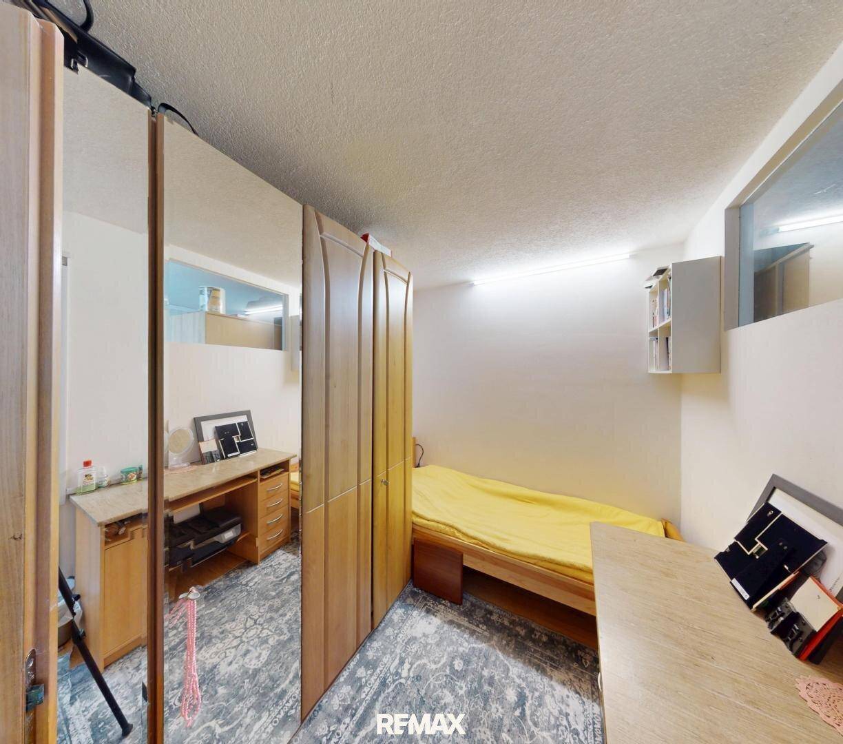 Schlafzimmer mit Einzelbett, Holzschrank und Schreibtisch.