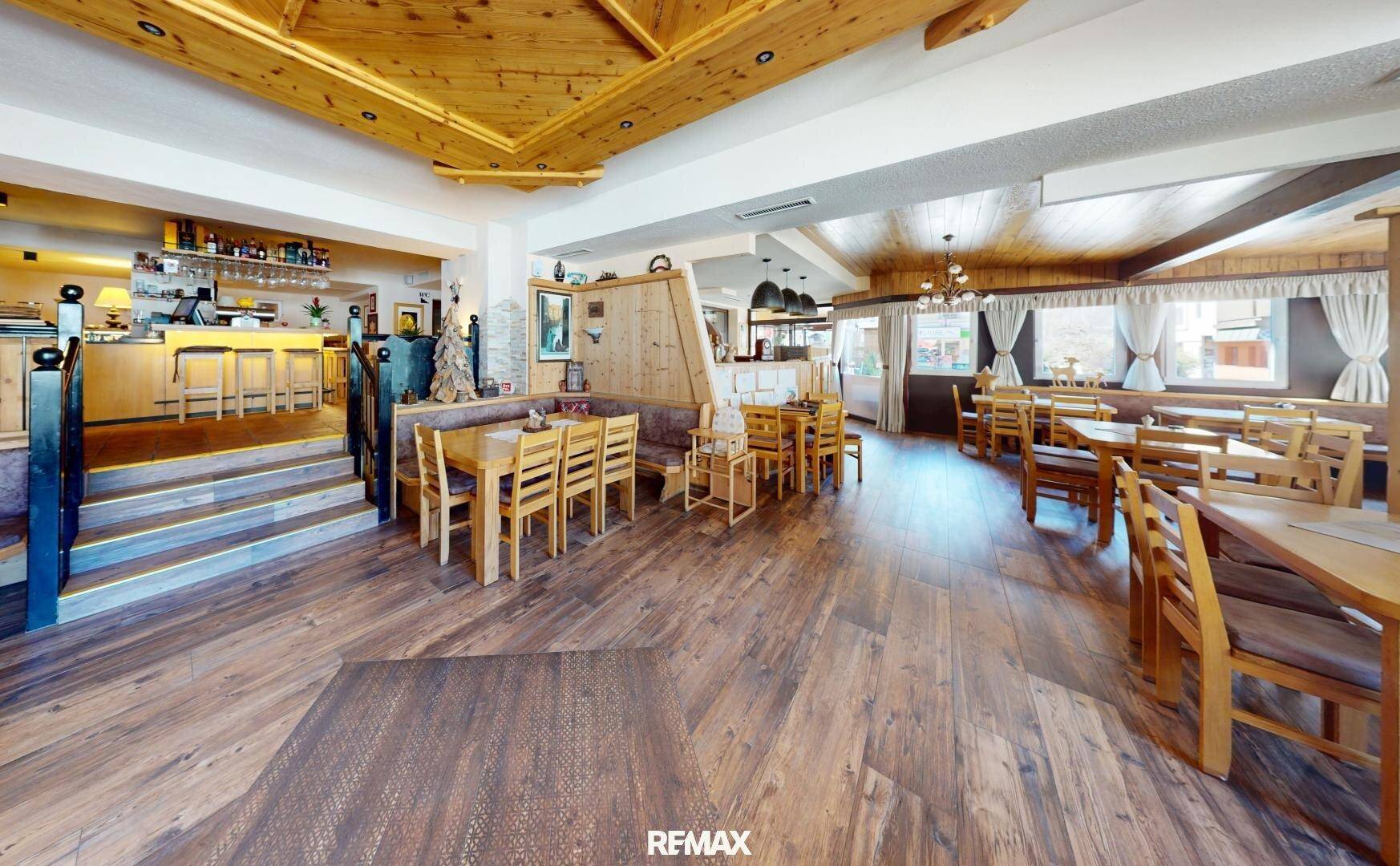 Geräumiger Speisesaal mit Holztischen und -stühlen, Holzboden und Blick auf den Barbereich.