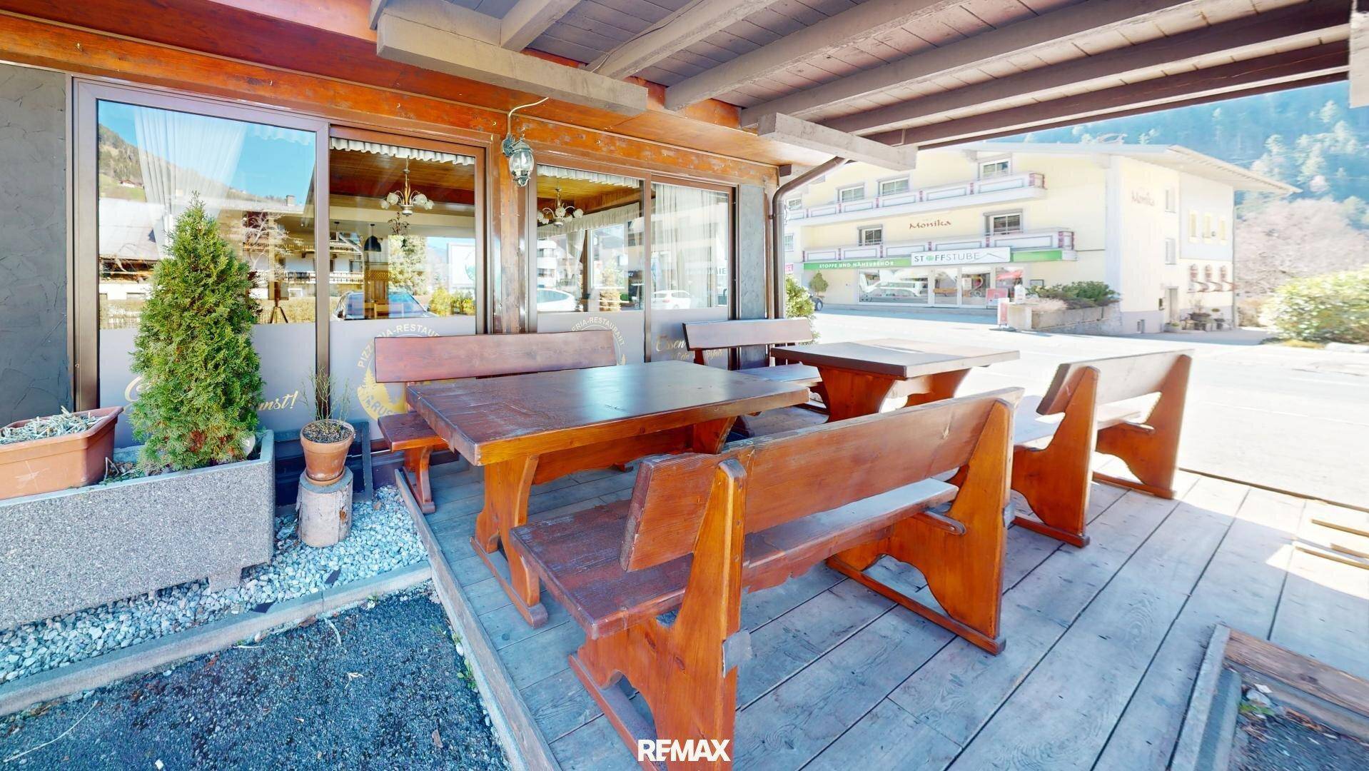 Rustikale Außenterrasse mit Holzbänken und Tischen, ideal für Mahlzeiten im Freien.