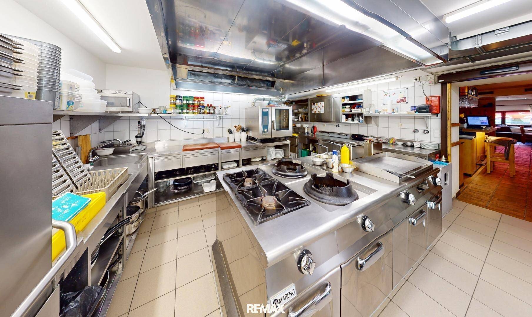 Große professionelle Küche mit Edelstahlgeräten, Gasherd und Fliesenboden für den Gastronomiebetrieb.